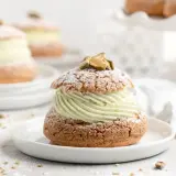 Un délice aérien : une religieuse garnie d'une crème onctueuse à la pistache, saupoudrée de sucre glace et décorée de pistaches.