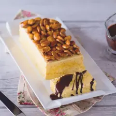 Gâteau rectangulaire glacé, garni d'amandes fruit caramélisées. Une part coupée est arrosée de sauce chocolat.