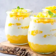 Délicieux dessert printemps en verrine, alternant couches de yaourt crémeux et de mangue fraîche, garni de dés de mangue et d'une feuille de menthe.