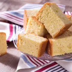 Tranches de madeira cake dorées et moelleuses, empilées sur une assiette en verre, avec une serviette rayée.