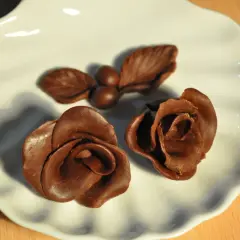 Deux roses et une petite branche avec des baies, le tout en chocolat plastique, sur une assiette blanche.