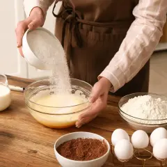 Préparation d'un gâteau : ajout de sucre dans un mélange d'œufs. On voit aussi du lait, de la farine, du cacao et du chocolat, des ingrédients pour savoir par quoi remplacer le lait dans un gâteau.