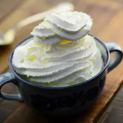 Une tasse bleue remplie de chantilly maison, prête à être dégustée avec une cuillère dorée en arrière-plan.