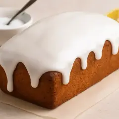 Glaçage au sucre glace et eau dégoulinant sur un cake doré. Une tranche de citron et un bol de glaçage sont à proximité.