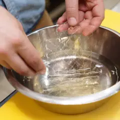 Mains trempant une feuille de gélatine dans l'eau froide. C'est la première étape pour savoir comment utiliser la gélatine en feuille.
