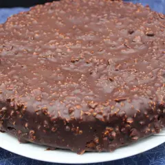 Gâteau rond au chocolat avec un glaçage rocher croustillant parsemé de noisettes concassées. Un délice gourmand.