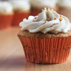 Un cupcake orné d'une généreuse ganache chocolat blanc, parsemé de perles rosées, dans un élégant caissette orange.