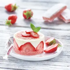 Délicieux gâteau biscuit aux fraises, garni de crème et de fruits frais, sur une assiette blanche avec des fraises éparpillées.