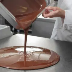 Un chef verse du chocolat fondu, illustrant la différence entre le beurre de cacao et le mycryo pour un tempérage parfait.