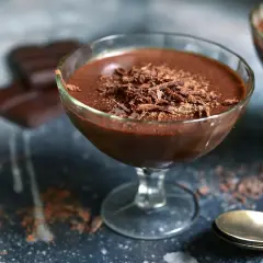 Délicieuse mousse chocolat entremet, garnie de copeaux de chocolat, servie dans un verre. Des carrés de chocolat sont flous en arrière-plan.