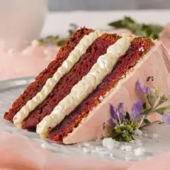 Tranche de gâteau Red Velvet avec une garniture molly cake crémeuse, décorée de fleurs violettes et de sucre glace.