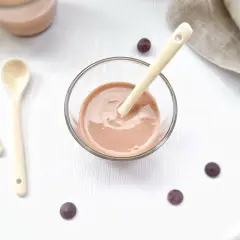Un bol de ganache praliné onctueuse, prêt à être dégusté avec une cuillère. Quelques pépites de chocolat parsèment la table.