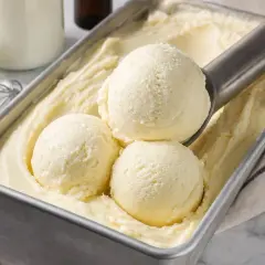 Une cuillère prélève des boules de glace à la vanille dans un bac. Une recette glace maison parfaite pour l'été.