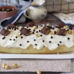 Gâteau moelleux recouvert de crème fouettée, décoré de morceaux de Kinder Bueno, noisettes et billes chocolatées. Un délice gourmand !