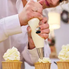 Pâtissière décorant des cupcakes avec une poche à douille. La crème est d'une belle couleur ivoire, parfaite pour savoir quel colorant pour chantilly mascarpone utiliser.