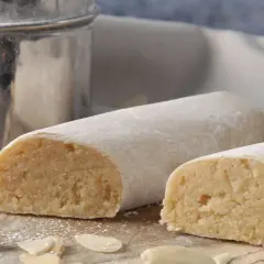 Pâte d'amande, c'est quoi ? Deux rouleaux de massepain, saupoudrés de sucre glace, sur une planche en bois, entourés d'amandes effilées.
