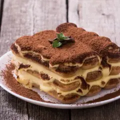 Un délicieux tiramisu, dont l'origine italienne est évidente, saupoudré de cacao, sur une assiette blanche.