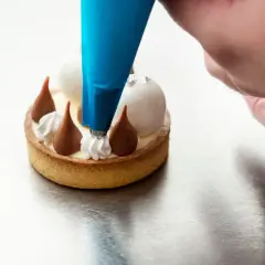 Un chef utilise une poche à douille bleue pour le pochage d'une crème sur un petit gâteau.