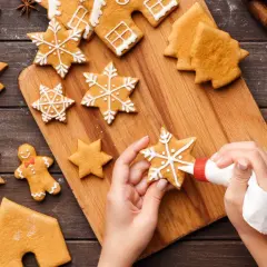 Mains décorant des sablés en forme d'étoiles et de sapins avec du glaçage blanc. Préparation de sablés avec glaçage pour les fêtes.