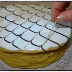 Un millefeuille rond, garni de crème pâtissière et décoré de glaçage blanc et chocolat, est finalisé avec une pique en bois.