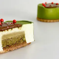 Entremet pistache aux couches délicates de mousse blanche, de crémeux et de biscuit croustillant, décoré de fruits rouges.