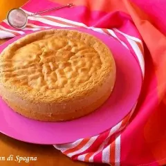 Un gâteau "Pan di Spagna" sur une assiette rose, prêt pour la conservation génoise. Un tamis est à côté.