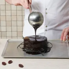 Un chef verse un glaçage au chocolat brillant sur un gâteau, créant le meilleur glaçage pour décorer un gâteau.
