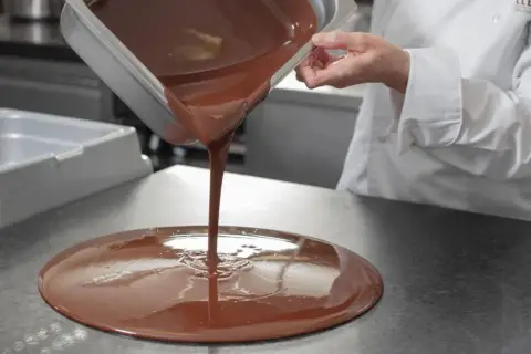 Un chef verse du chocolat fondu, illustrant la différence entre le beurre de cacao et le mycryo pour un tempérage parfait.