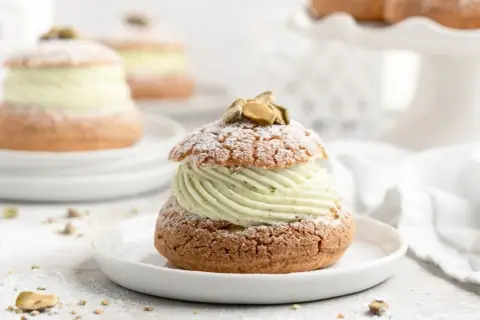 Un délice aérien : une religieuse garnie d'une crème onctueuse à la pistache, saupoudrée de sucre glace et décorée de pistaches.