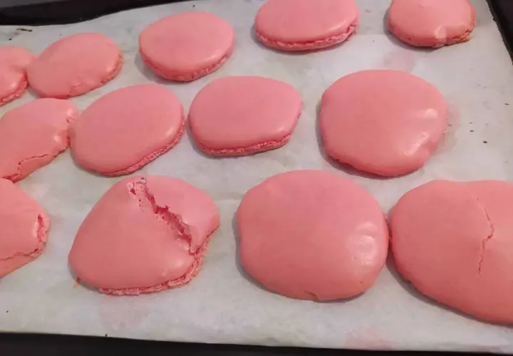 Des macarons roses sur une plaque de cuisson. Certains sont craquelés, un mystère pour comprendre pourquoi mes macarons craquent.