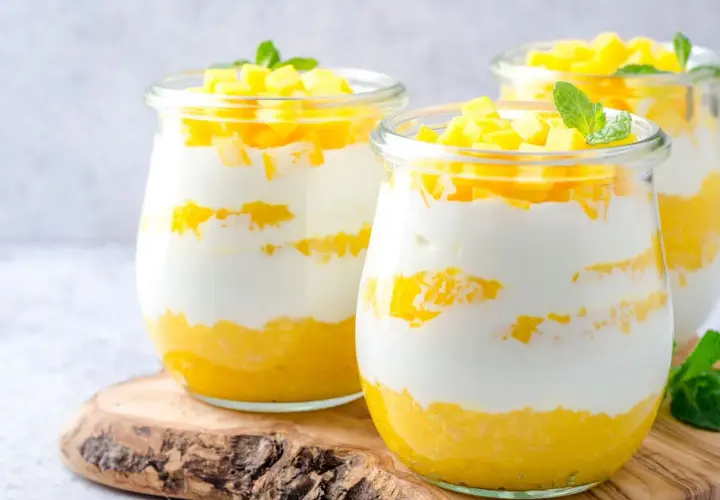 Délicieux dessert printemps en verrine, alternant couches de yaourt crémeux et de mangue fraîche, garni de dés de mangue et d'une feuille de menthe.