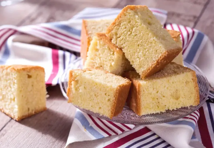 Tranches de madeira cake dorées et moelleuses, empilées sur une assiette en verre, avec une serviette rayée.