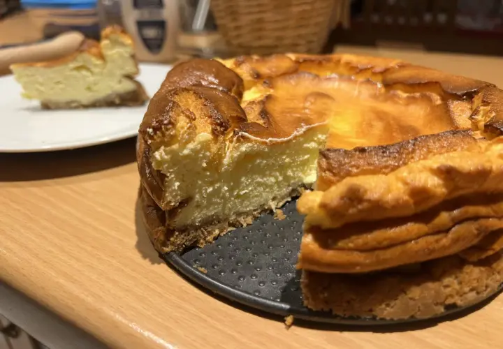 Un délicieux gâteau healthy, un cheesecake doré et crémeux, avec une part déjà servie sur une assiette blanche.