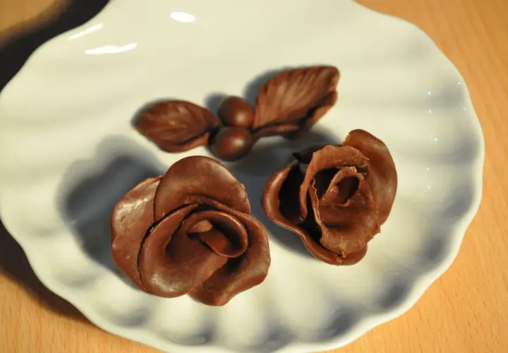 Deux roses et une petite branche avec des baies, le tout en chocolat plastique, sur une assiette blanche.