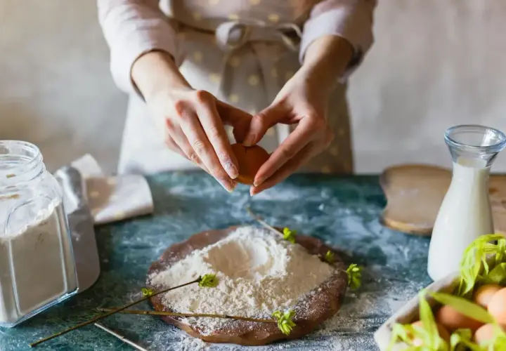 Mains préparant un œuf pour des ingrédients de pâtisserie. Farine, lait et œufs sont prêts pour la création d'une recette.