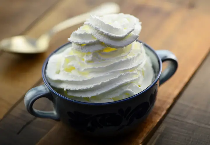 Une tasse bleue remplie de chantilly maison, prête à être dégustée avec une cuillère dorée en arrière-plan.