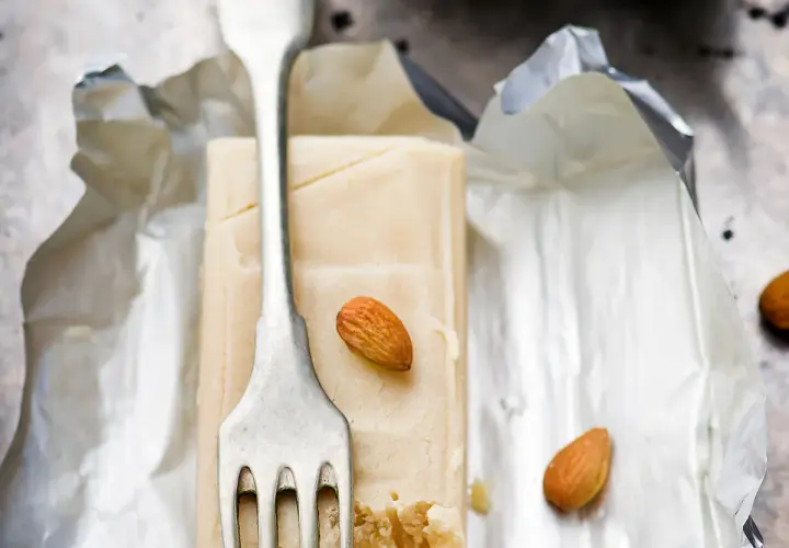 Bloc de pâte d'amande pour recouvrir un gâteau, avec une fourchette et des amandes.