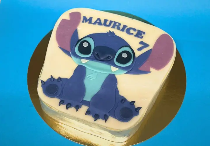 Gâteau thème Stitch pour Maurice, qui fête ses 7 ans. Le personnage bleu est assis sur un glaçage blanc.