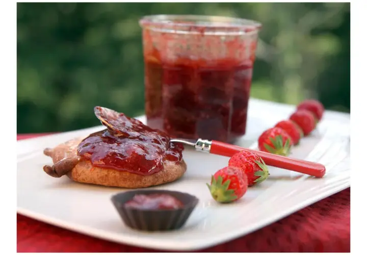 Confiture de framboise pectine sur un biscuit, avec des fraises fraîches alignées.