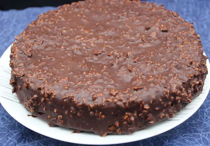 Gâteau rond au chocolat avec un glaçage rocher croustillant parsemé de noisettes concassées. Un délice gourmand.