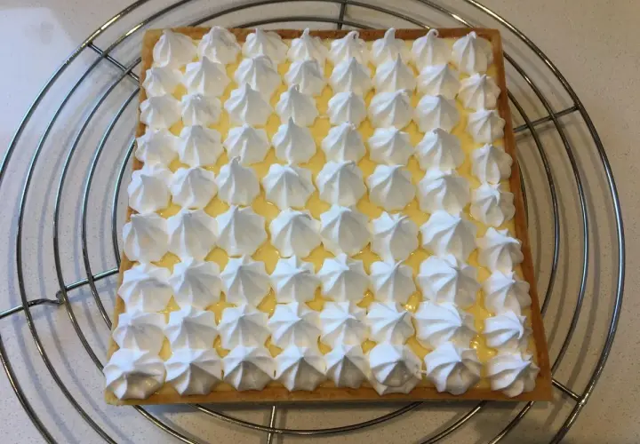 Tarte citron meringuée rectangulaire, garnie de crème citron et de petites meringues blanches disposées en grille. Un délice signé Pierre Hermé.