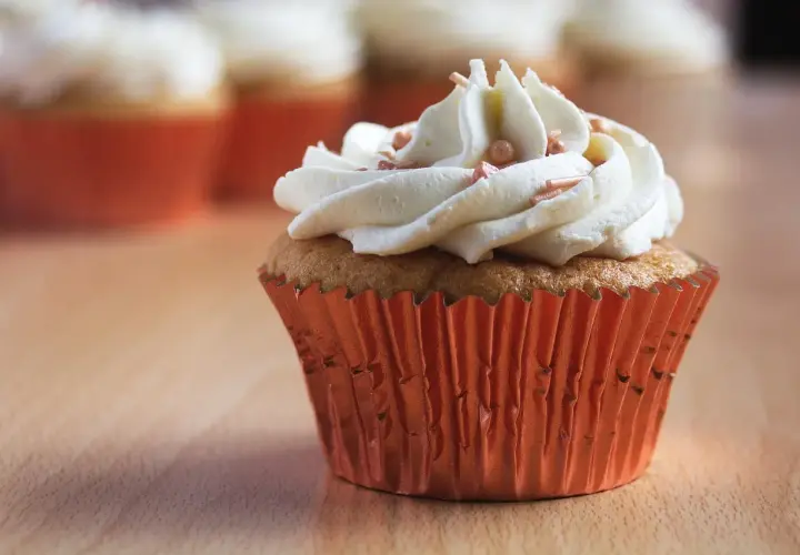 Un cupcake orné d'une généreuse ganache chocolat blanc, parsemé de perles rosées, dans un élégant caissette orange.