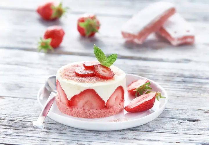 Délicieux gâteau biscuit aux fraises, garni de crème et de fruits frais, sur une assiette blanche avec des fraises éparpillées.