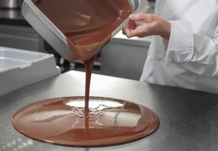 Un chef verse du chocolat fondu, illustrant la différence entre le beurre de cacao et le mycryo pour un tempérage parfait.
