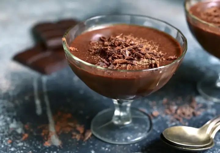Délicieuse mousse chocolat entremet, garnie de copeaux de chocolat, servie dans un verre. Des carrés de chocolat sont flous en arrière-plan.