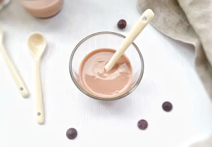 Un bol de ganache praliné onctueuse, prêt à être dégusté avec une cuillère. Quelques pépites de chocolat parsèment la table.