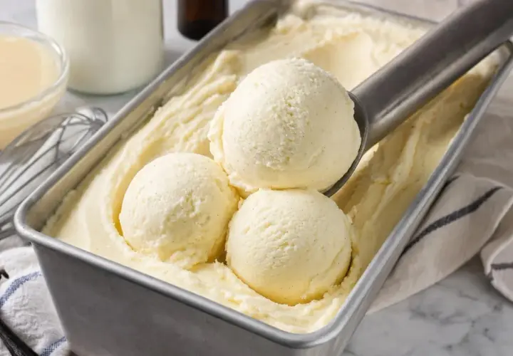 Une cuillère prélève des boules de glace à la vanille dans un bac. Une recette glace maison parfaite pour l'été.