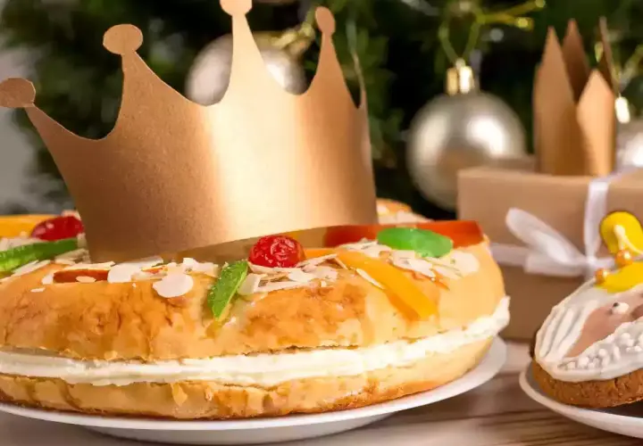 Un roi porte une couronne dorée sur un délicieux gâteau praliné, décoré de fruits confits et d'amandes. Un cadeau emballé et des décorations de Noël en arrière-plan.