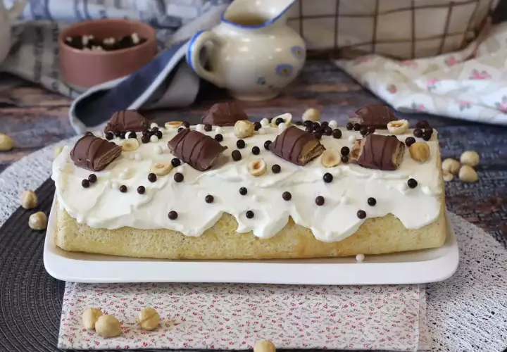 Gâteau moelleux recouvert de crème fouettée, décoré de morceaux de Kinder Bueno, noisettes et billes chocolatées. Un délice gourmand !