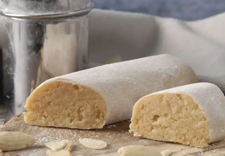 Pâte d'amande, c'est quoi ? Deux rouleaux de massepain, saupoudrés de sucre glace, sur une planche en bois, entourés d'amandes effilées.